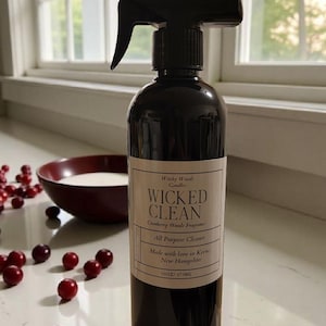 Pode incluir: Um borrifador castanho escuro com o rótulo "WICKED CLEAN", "Cranberry Woods Fragrance" e "All Purpose Cleaner". A garrafa tem 473 ml. Arandos frescos e uma tigela vermelha em primeiro plano.