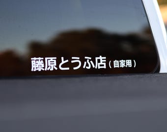以下が含まれることがあります： 車の窓に貼られた、日本語のテキストが入った白いビニールステッカー。テキストは「藤原とうふ店（自家用）」と書かれています。ステッカーは暗い表面にあり、背景はぼやけています。