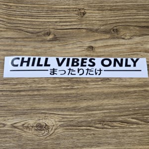 May include: A white sticker with the text "CHILL VIBES ONLY" in a bold, black font. Below the English text is Japanese text. The sticker is rectangular and placed on a wooden surface.