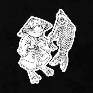 Puede incluir: Adhesivo en blanco y negro que representa una rana con un sombrero y una túnica japoneses tradicionales, sosteniendo un pez grande. La rana y el pez están dibujados con líneas detalladas. Fondo negro.