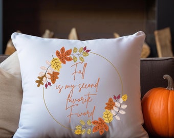 May include: Square white cushion with a fall-themed design. The cushion has a gold-coloured circular frame with colourful leaves and the text "Fall is my second favourite F-word" in orange script. An orange pumpkin sits to the right.