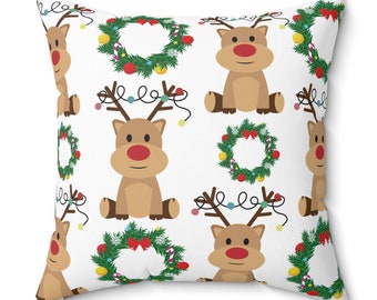 May include: Square white pillow with a repeating pattern of cartoon reindeer with red noses and Christmas wreaths. The reindeer have brown antlers and are decorated with string lights. A festive holiday home decor item.