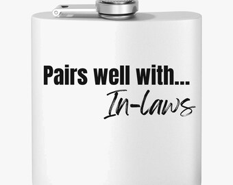 Może przedstawiać: Biała piersiówka ze srebrną nakrętką i zawiasem. Na piersiówce znajduje się czarny napis "Pairs well with... In-laws".