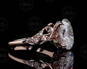 May include: A rose gold ring featuring a large oval-cut center stone and a band designed with intricate leaf motifs and small round accent stones. The metal has a warm metallic finish, and the setting displays detailed organic vine-like textures.