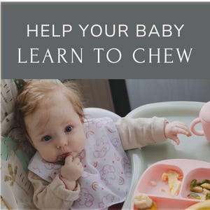 May include: A baby wearing a pink and white bib with a rainbow and cloud design is sitting in a high chair and eating. The baby is holding a piece of food in their hand and is looking at the camera. The baby is sitting in front of a pink and green divided plate with food on it.