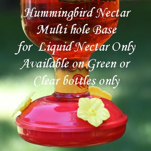 May include: A hummingbird feeder with a red base and yellow flower-shaped feeding ports. The text reads: Hummingbird Nectar, Multi hole Base, for Liquid Nectar Only, Available on Green or Clear bottles only. The bottle contains red liquid.