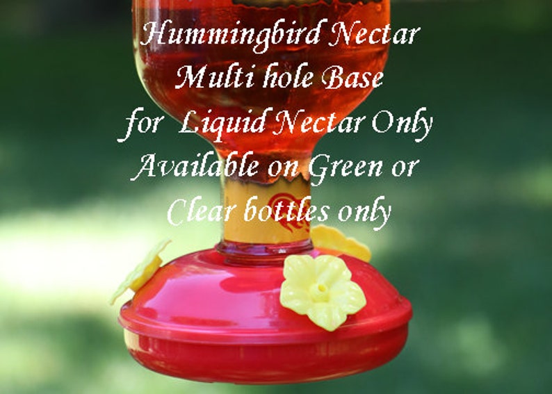 Op de afbeelding: Een kolibrie-voederbak met een rode basis en gele bloemvormige voeropeningen. De tekst luidt: Hummingbird Nectar, Multi hole Base, for Liquid Nectar Only, Available on Green or Clear bottles only. De fles bevat een rode vloeistof.