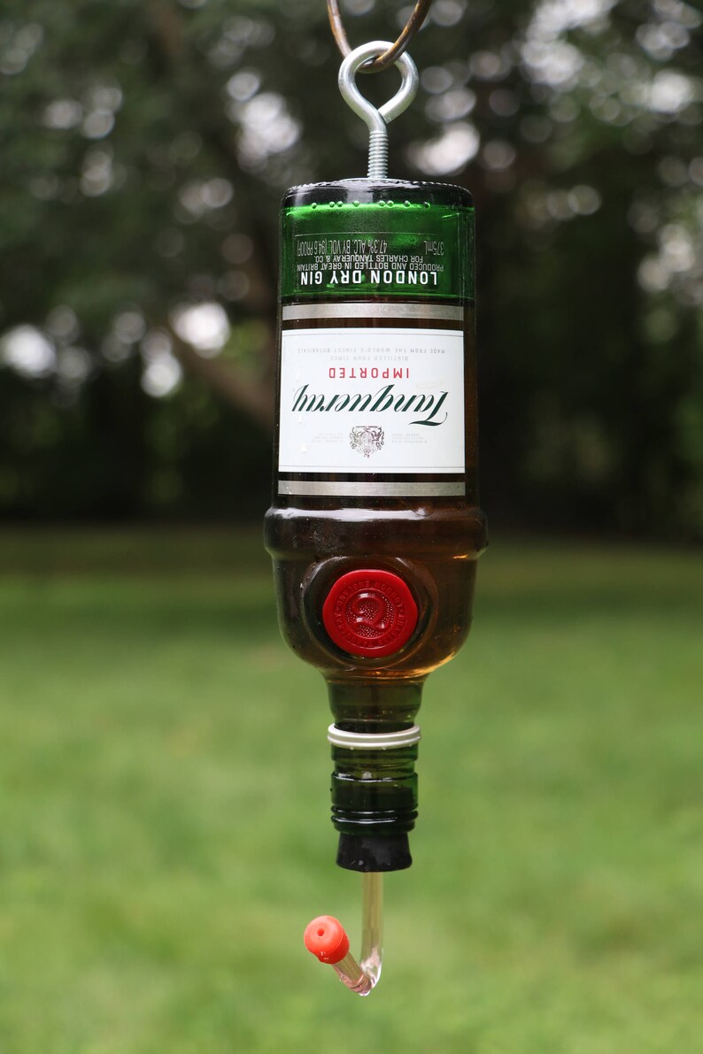 May include: A repurposed Tanqueray London Dry Gin bottle, inverted and fitted with a red stopper and a clear tube. The bottle is suspended by a metal hook. The label reads "Tanqueray Imported London Dry Gin".