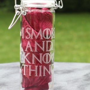May include: A clear glass jar with a silver lid and a red cloth inside. The jar has the words "I smoke and I know things" etched on the side.