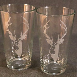 May include: Two clear glass pint glasses with an etched design of a deer head with antlers.