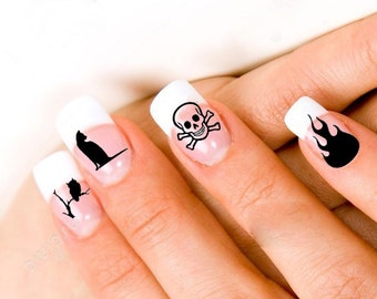 Puede incluir: Primer plano de una mano con cuatro uñas pintadas de blanco con diseños negros. Los diseños incluyen una calavera y huesos cruzados, un gato, un pájaro en una rama y llamas.