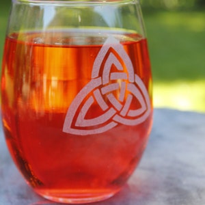 May include: A clear glass wine glass with a red liquid inside. The glass has a Celtic knot design etched into the side.