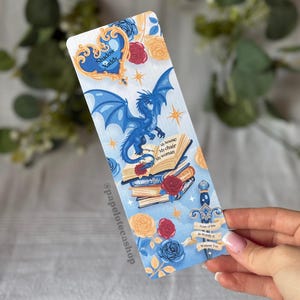 Puede incluir: Marcapáginas de fantasía con un dragón azul, rosas y libros. El marcapáginas tiene un fondo azul y blanco con el texto "Shadow Xaddy" y "None of this is Worth it Without You."