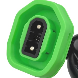 Puede incluir: Primer plano de un conector eléctrico verde y negro. La carcasa verde tiene forma hexagonal, enmarcando un puerto rectangular negro con múltiples pines. Un cable negro se extiende desde el conector.