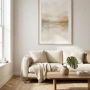 May include: A framed abstract landscape art print in neutral tones hangs above a cream-colored sofa. The artwork features a watercolor-style depiction of a serene waterscape. A wooden coffee table, rug, and decorative items complete the living room setting.