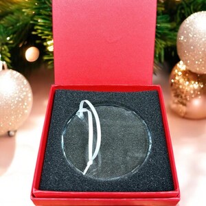May include: A clear glass ornament with a white string hanger, in a red box with black foam padding.