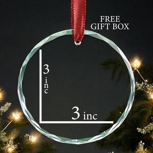 May include: A clear glass ornament with a 3 inch diameter. The ornament is round and has a faceted edge. It is hanging from a red ribbon.