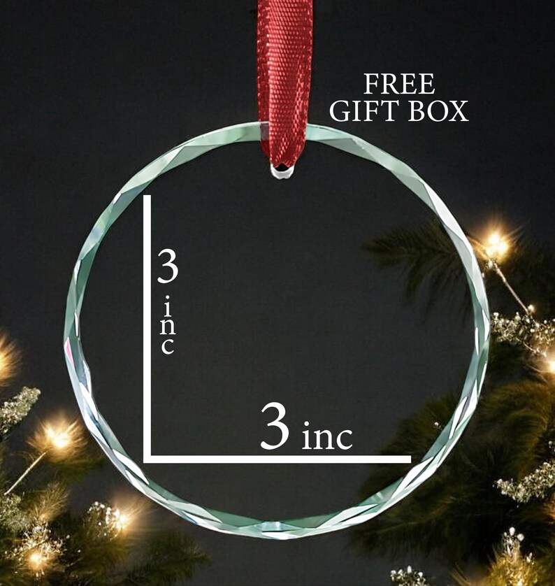 May include: A clear glass ornament with a 3 inch diameter. The ornament is round and has a faceted edge. It is hanging from a red ribbon.