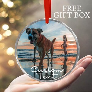 May include: Round glass ornament with a photo of a dog and a person on a beach. The ornament has a white border with the text "Custom Text" printed on it.