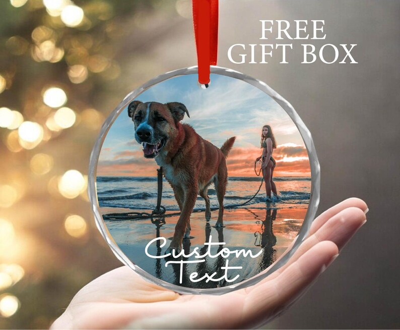 May include: Round glass ornament with a photo of a dog and a person on a beach. The ornament has a white border with the text "Custom Text" printed on it.