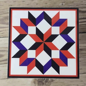May include: A square, white background with a red, black, and purple geometric pattern. The pattern is a quilt block design with a star shape in the centre.