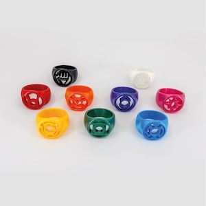 May include: A collection of nine rings in various colors including red, orange, yellow, green, blue, purple, pink, black, and white. Each ring features a distinct circular emblem cutout on the front face, representing different power symbols.