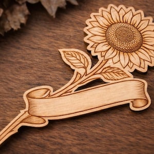 Puede incluir: Artesanía de madera con forma de girasol con una pancarta para personalizar. El girasol tiene grabados detallados de pétalos y centro. La pancarta está en blanco, lista para texto personalizado. Hecho de madera clara.