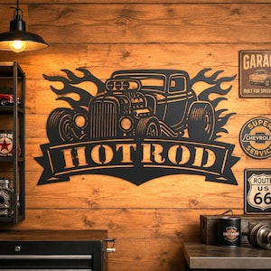 Op de afbeelding: Zwart metalen wandkunst met een hot rod auto-ontwerp met vlammen en het woord "HOTROD" in een banner. Het kunstwerk is gemonteerd op een houten muur, met vintage borden en een plank met decor.