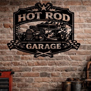 Puede incluir: Letrero de metal negro con las palabras "HOT ROD GARAGE" y un diseño de coche hot rod clásico. El letrero presenta llamas, banderas a cuadros y llaves cruzadas, montado en una pared de ladrillo.