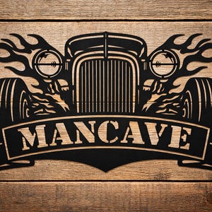 May include: Black metal wall art featuring a classic hot rod design with flames and the word "MANCAVE" in a banner. The artwork is mounted on a wooden background, creating a rustic aesthetic. Ideal for a garage or man cave.