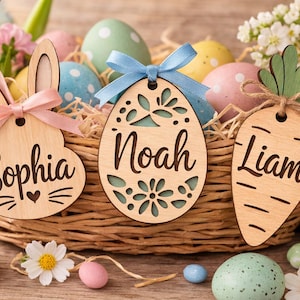 Könnte beinhalten: Ein Weidenkorb gefüllt mit dekorierten Ostereiern und Namensschildern aus Holz. Die Schilder sind in Form eines Hasen, eines Eies und einer Karotte gehalten, jedes mit einem Namen. Pastellfarbene Eier und Blumen umgeben den Korb.