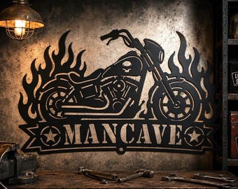 May include: Black metal motorcycle wall art with a skull on the engine, surrounded by flames. The word "MANCAVE" is displayed below the motorcycle. The art is mounted on a textured wall, with a vintage lamp above.