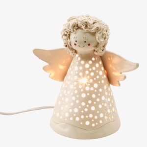 Può includere: Una statuetta di angelo in ceramica bianca con una luce all'interno. L'angelo ha un motivo a pois e un viso sorridente. La statuetta è illuminata dall'interno, creando un bagliore caldo.