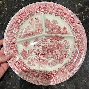 May include: A divided plate with a red and white Willow pattern design. The plate features three compartments and a decorative border. The pattern depicts a landscape with buildings, trees, and a bridge.
