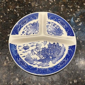May include: A round, divided serving plate with a blue and white Willow pattern. The plate has three sections and a scalloped edge. The blue design features a landscape with buildings, trees, and a bridge.