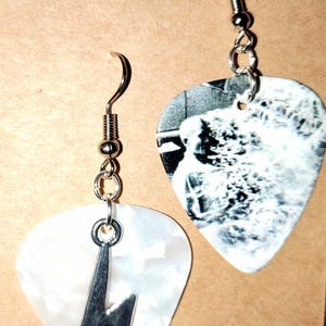 May include: A pair of mismatched earrings featuring guitar pick charms. One earring has a white pearlescent guitar pick with a silver-toned lightning bolt charm attached. The other earring features a guitar pick with a black and white graphic print.