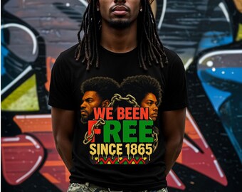Può includere: Una persona che indossa una maglietta nera con una grafica di due volti di uomini neri e il testo "WE BEEN FREE SINCE 1865". La persona indossa una bandana sulla testa e ha i dreadlocks.