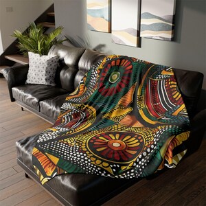 May include: A black throw blanket with a vibrant, colorful pattern featuring red, yellow, green, and white geometric designs. The blanket is draped over a black leather sofa, adding a decorative touch to the living space.