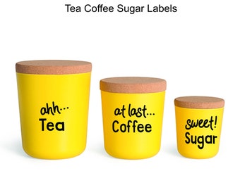 May include: Three yellow canisters with cork lids and black labels. The labels read "ahh... Tea", "at last... Coffee", and "sweet! Sugar".