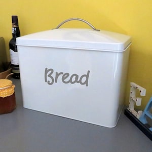 May include: White metal bread bin with a silver handle and the word "Bread" written in grey on the front.