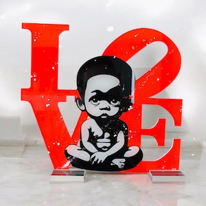 Puede incluir: Una escultura de acrílico rojo de la palabra "LOVE" con una ilustración en blanco y negro de un niño sentado en el centro de la "O".