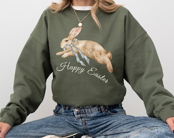 May include: A green sweatshirt with a watercolor illustration of a brown bunny with a blue ribbon. The text "Happy Easter" is printed below the bunny.