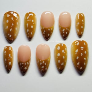 Puede incluir: Un juego de diez uñas postizas en forma de almendra con un patrón de puntos marrones y blancos. Algunas uñas están completamente cubiertas con el patrón marrón y blanco, mientras que otras presentan un diseño de punta francesa nude. El texto pressonhaven es visible.