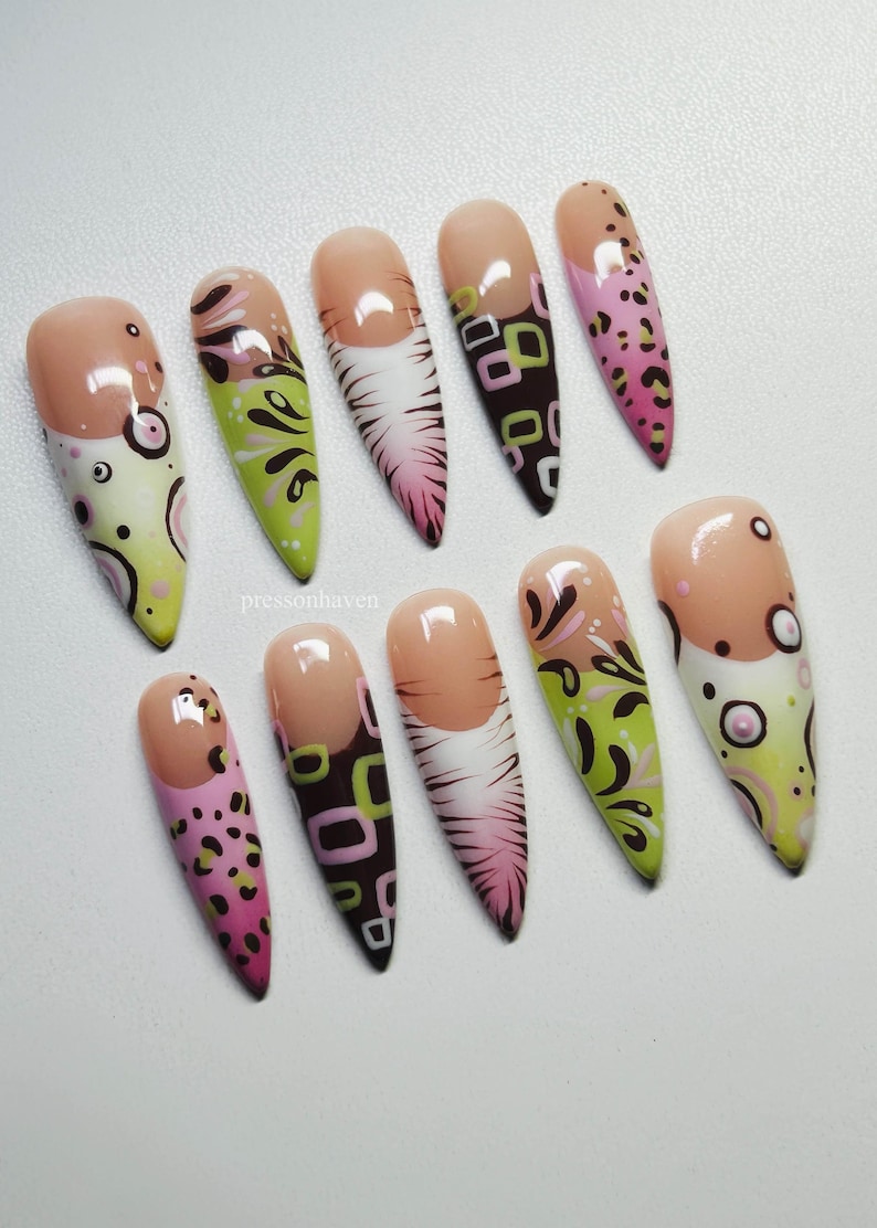 Puede incluir: Un conjunto de diez u&ntilde;as postizas largas en forma de almendra. Cada u&ntilde;a presenta una base nude y varios dise&ntilde;os, incluyendo estampado de leopardo rosa, espirales verdes y negras y patrones geom&eacute;tricos en marr&oacute;n y verde. Las u&ntilde;as est&aacute;n dispuestas sobre una superficie blanca.