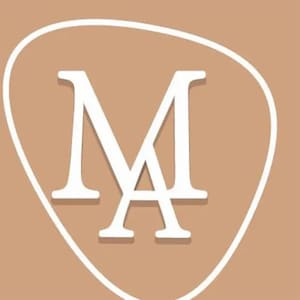 以下が含まれることがあります： 薄い茶色の背景に、白い楕円形の中に白い文字「MA」が入っています。