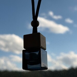 May include: A blue glass car air freshener with a wooden top, hanging from a black string.