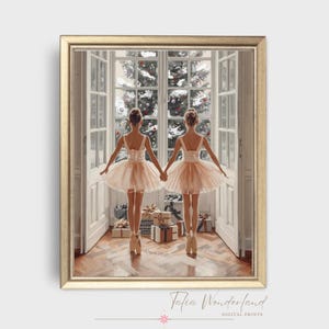 Op de afbeelding: Een ingelijste print met twee ballerina's in perzikkleurige tutu's, hand in hand, kijkend door een raam naar een kerstboom. De print heeft een gouden lijst en de tekst "Talia Wonderland DIGITAL PRINTS" onderaan.