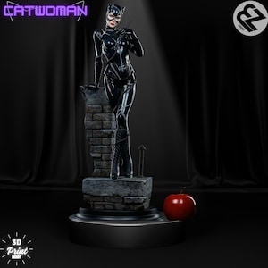 May include: A black and gray 3D printed figurine of Catwoman standing on a brick ledge. She is wearing a black leather suit with a catsuit and a black mask. She is holding a whip in her right hand. The figurine is on a black base with a red apple in front of it.