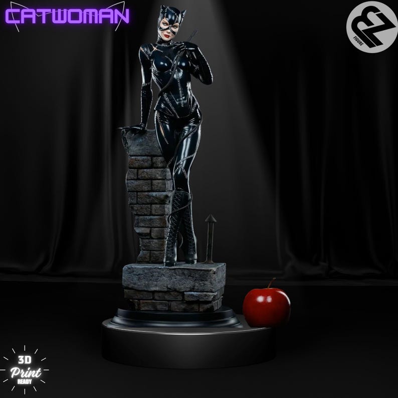 May include: A black and gray 3D printed figurine of Catwoman standing on a brick ledge. She is wearing a black leather suit with a catsuit and a black mask. She is holding a whip in her right hand. The figurine is on a black base with a red apple in front of it.