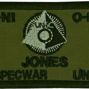 May include: A green military patch with the text "ONI O-POS JONES NAVSPECWAR UNSC" and a white and black emblem with a circle and triangle.